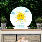 Wooden Baptism/candybar figure: happy sun boy with blue bow tie, "Our little Sunshine". White table, green backdrop.