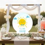 Wooden happy sun boy figure with bow tie for baptism candy bar. On wooden table with sweets, arch background.