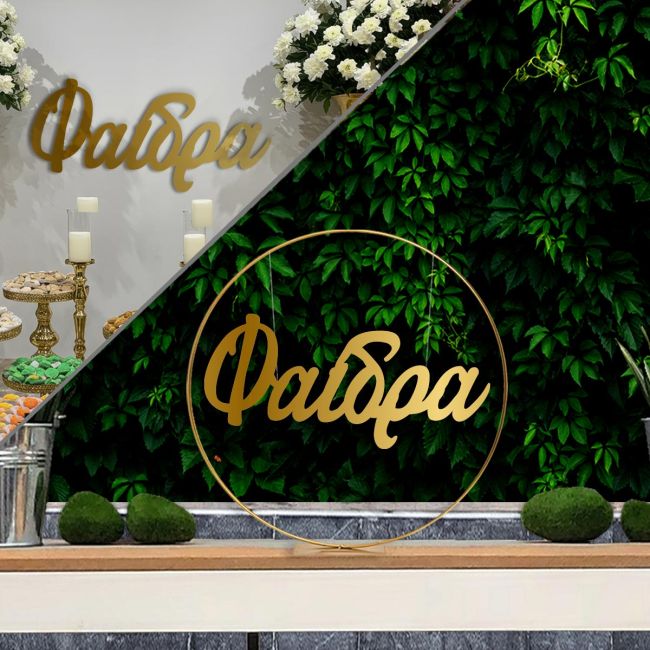 Gold metal baptism arch with hanging name 'Faidra' in gold plexiglass, against a plant background.