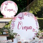 Round wooden candy bar sign with a pink flower and butterfly print, set behind a dessert table outdoors.