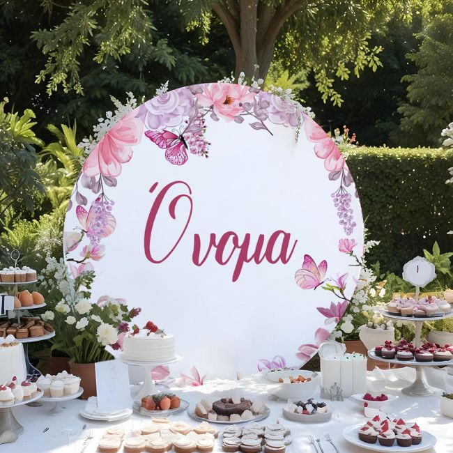 Στρογγυλή ξύλινη πινακίδα candy bar με ροζ λουλούδια και πεταλούδες, τοποθετημένη σε τραπέζι γλυκών σε κήπο.