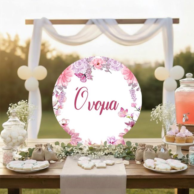 Κυκλική ξύλινη πινακίδα candy bar με ροζ λουλούδια και πεταλούδες, σε τραπέζι εξωτερικού χώρου.