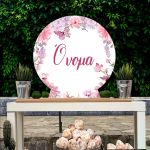 Ξύλινη στρογγυλή πινακίδα candy bar με ροζ λουλούδια και πεταλούδες, τοποθετημένη σε τραπέζι.