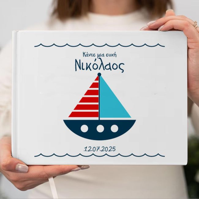 White hardcover wish book with blue-red sailboat, name Nikolaos. Woman holding the book.