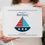 White hardcover wish book with blue-red sailboat, name Nikolaos. Woman holding the book.