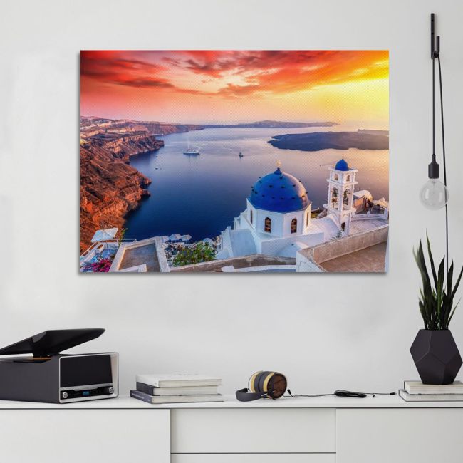 Photographic canvas: Santorini sunset, blue domes, red cliffs. Mounted on a white wall.