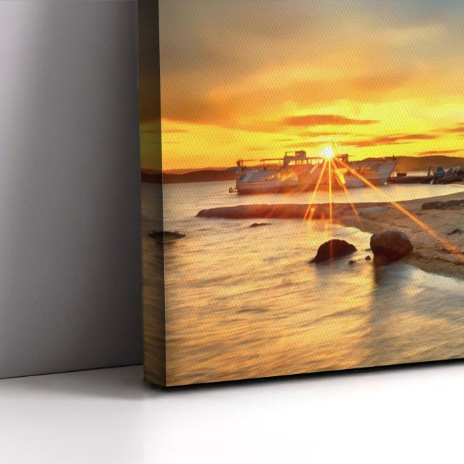 Canvas print: Sunset at sea, ferry, rocky shore. Art piece leaning on a grey wall.