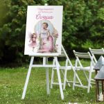 Christening canvas board with a fairy and photo, on a white wooden easel in a garden setting.