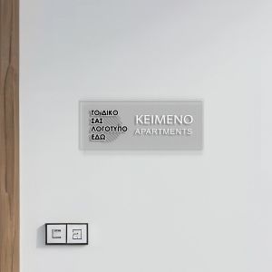 Διάφανη πινακίδα plexiglass με UV εκτύπωση, μοντέρνου στυλ, σε γκρι τοίχο μπετόν με μεταλλικούς αποστάτες. 2