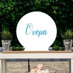 Wooden round white sign with blue 'Name' script, on candy bar table, green ivy background.