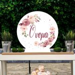 Στρογγυλή ξύλινη πινακίδα Candy Bar με ζωγραφιστά λουλούδια σε σάπιο μήλο, σε τραπέζι με φόντο πρασινάδα.