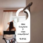 White door hanger 'The bride is getting ready', printed on plastic/cardstock, hanging on doorknob with bride in background.