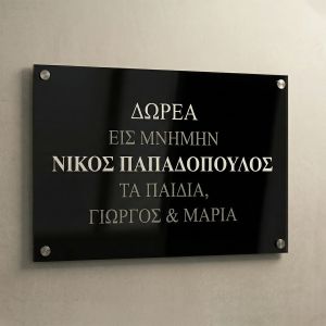 Commemorative plaque, black Plexiglass with UV printed silver text, wall-mounted with standoffs on a light wall.