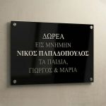 Πινακίδα μνήμης μαύρου Plexiglass, UV εκτύπωση ασημένια γράμματα, με στήριξη σε ανοιχτόχρωμο τοίχο.