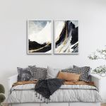 Diptych canvas print of abstract mountains with golden lines in white frames above a bed.
